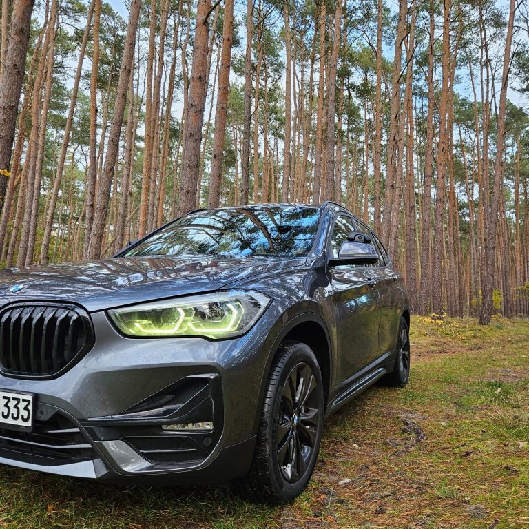 Der graue BMW X1 der Fahrschule Wahl auf einem Waldweg im Kiefernwald