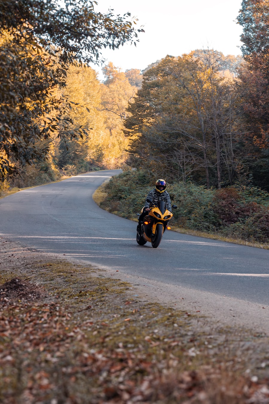 Motorradfahrer auf einer leeren Landstraße durch herbstlichen Laubwald