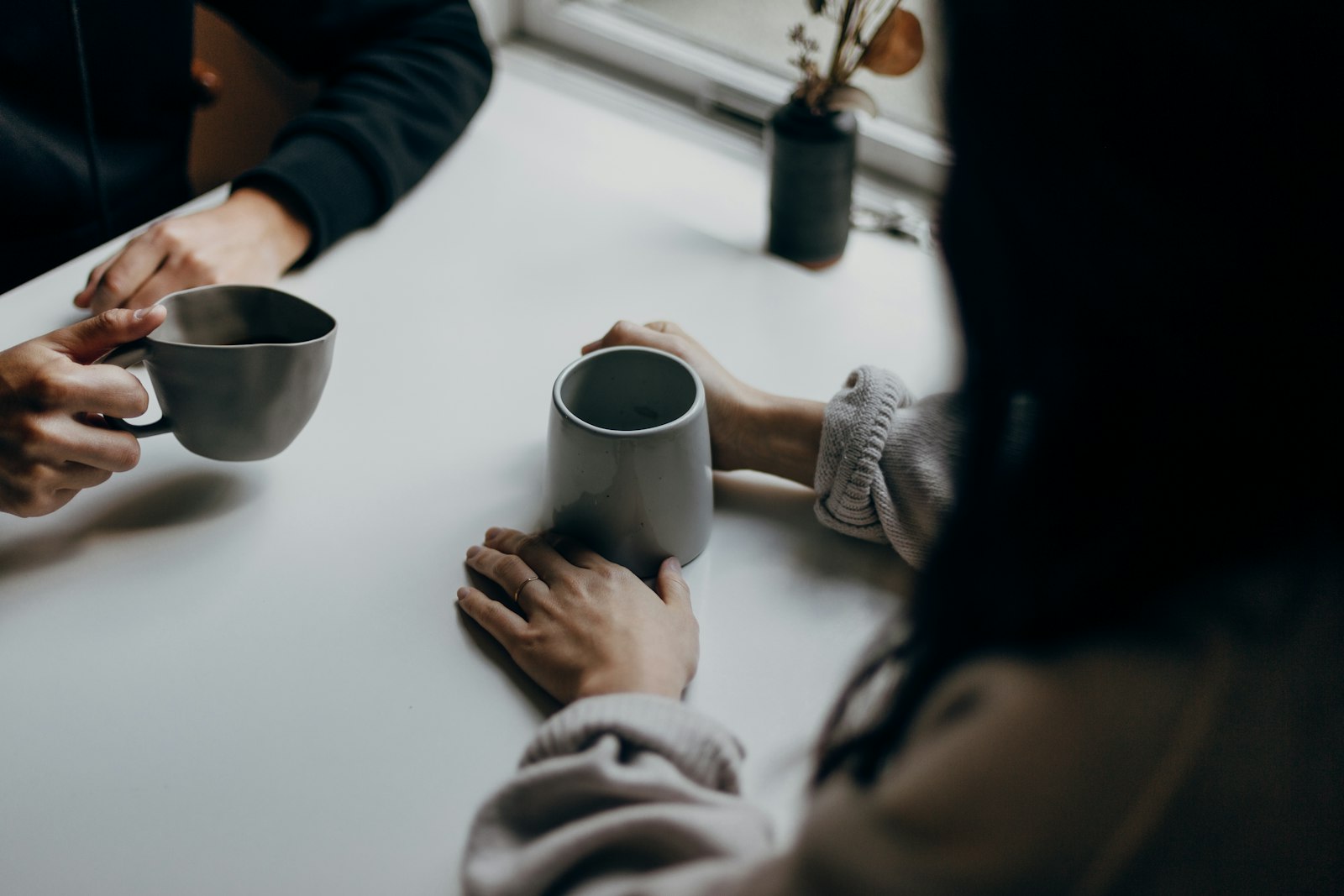 Zwei Menschen sitzen mit Kaffeetassen an einem Tisch und sprechen miteinander