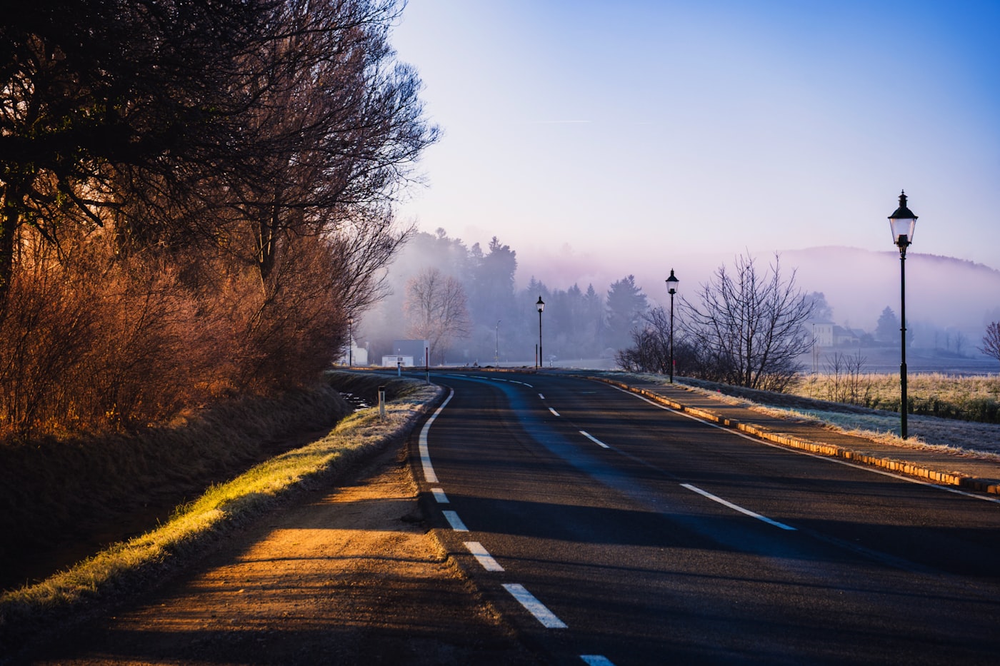 Leere Landstraße im Morgenlicht, der Nebel lichtet sich über den Feldern